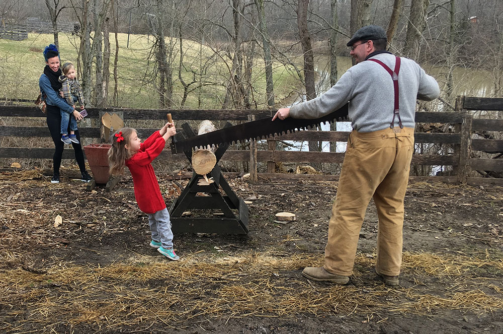 A farmer and child saw a log during a Slate Run Living Historical Farm program